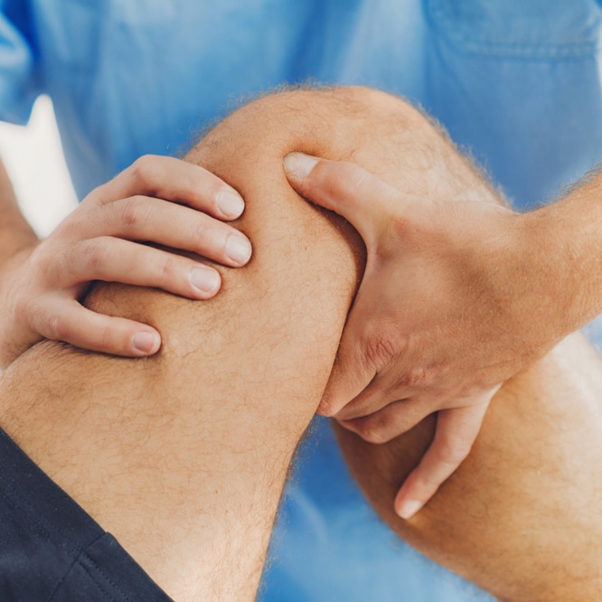 Osteopath treating male patient for knee pain