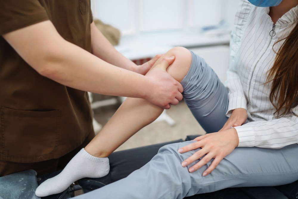Osteopath assessing female patient with leg pain